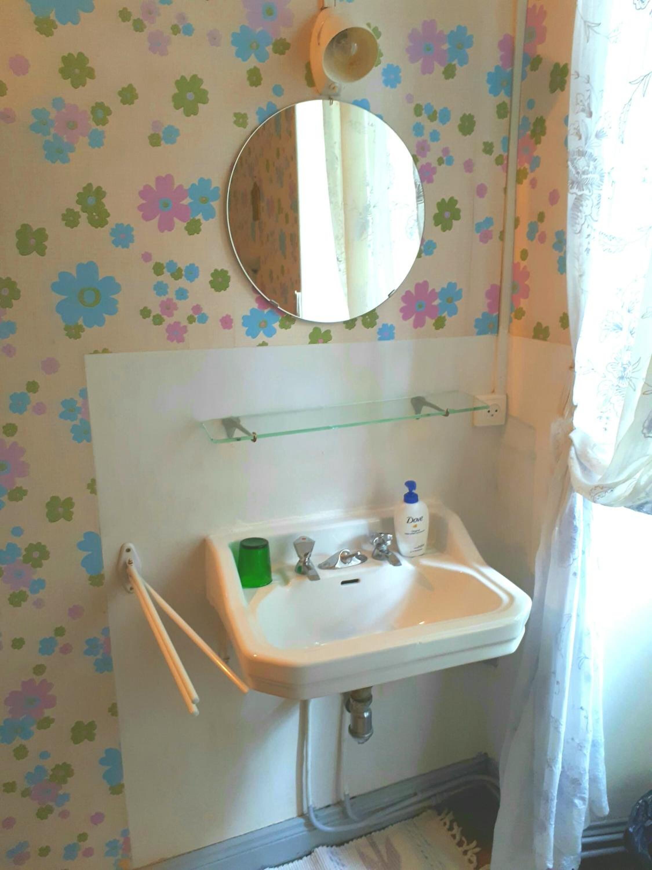 Un baño con un lavamanos blanco, un espejo y una estantería de vidrio arriba.