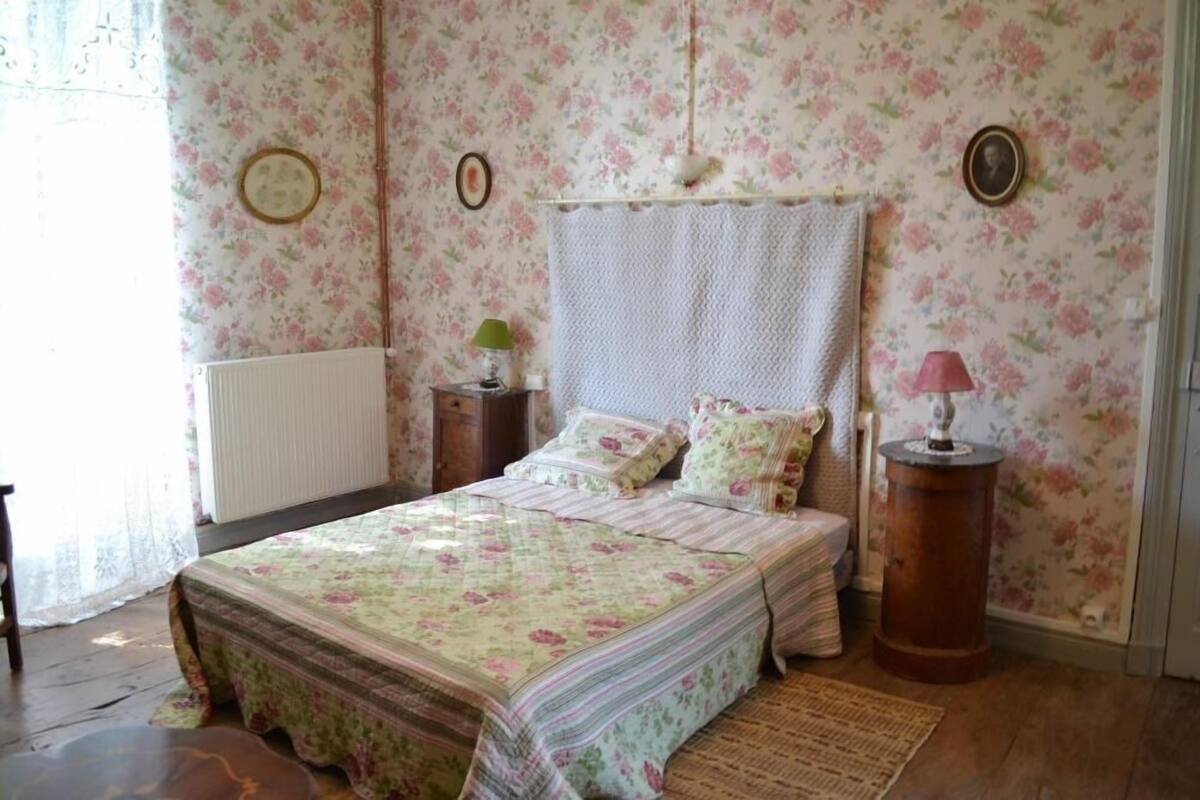 Une chambre avec un papier peint à motifs floraux, un lit avec une literie à motifs floraux, deux tables de chevet avec des lampes et un radiateur.