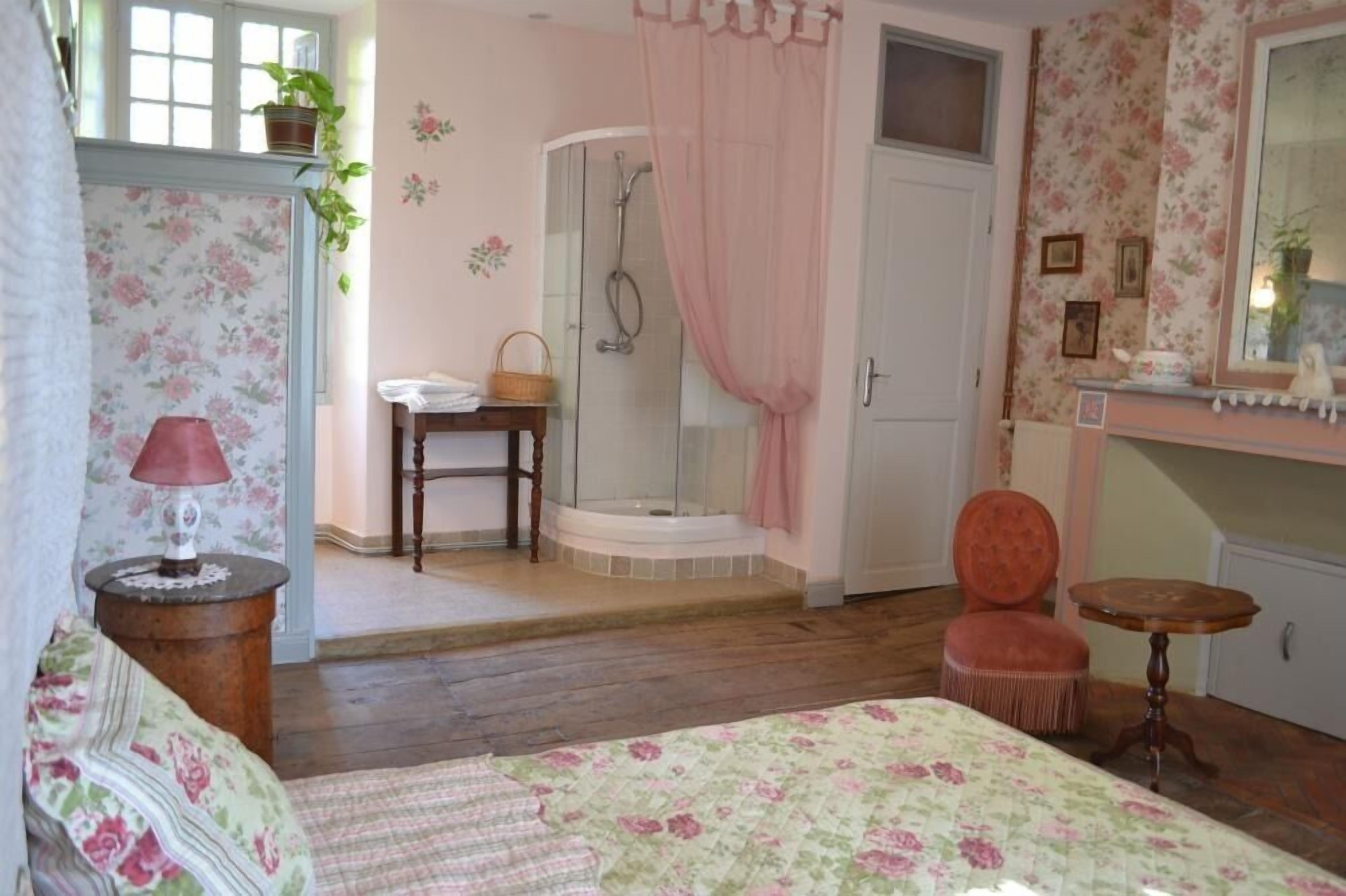 Una camera da letto con un letto, un comodino, una sedia, un tavolino, una doccia e un angolo trucco con uno specchio.