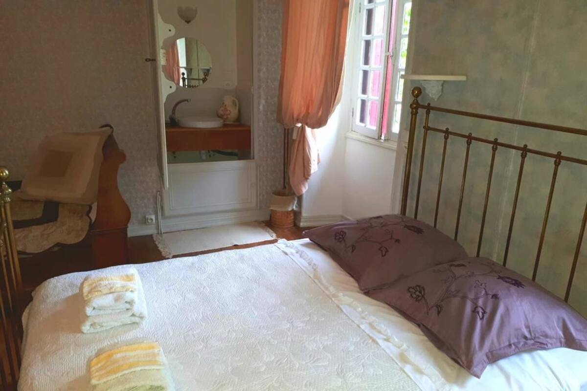 Une chambre à coucher avec un lit, une tête de lit en bois, une table de chevet, un miroir et une fenêtre avec des rideaux.