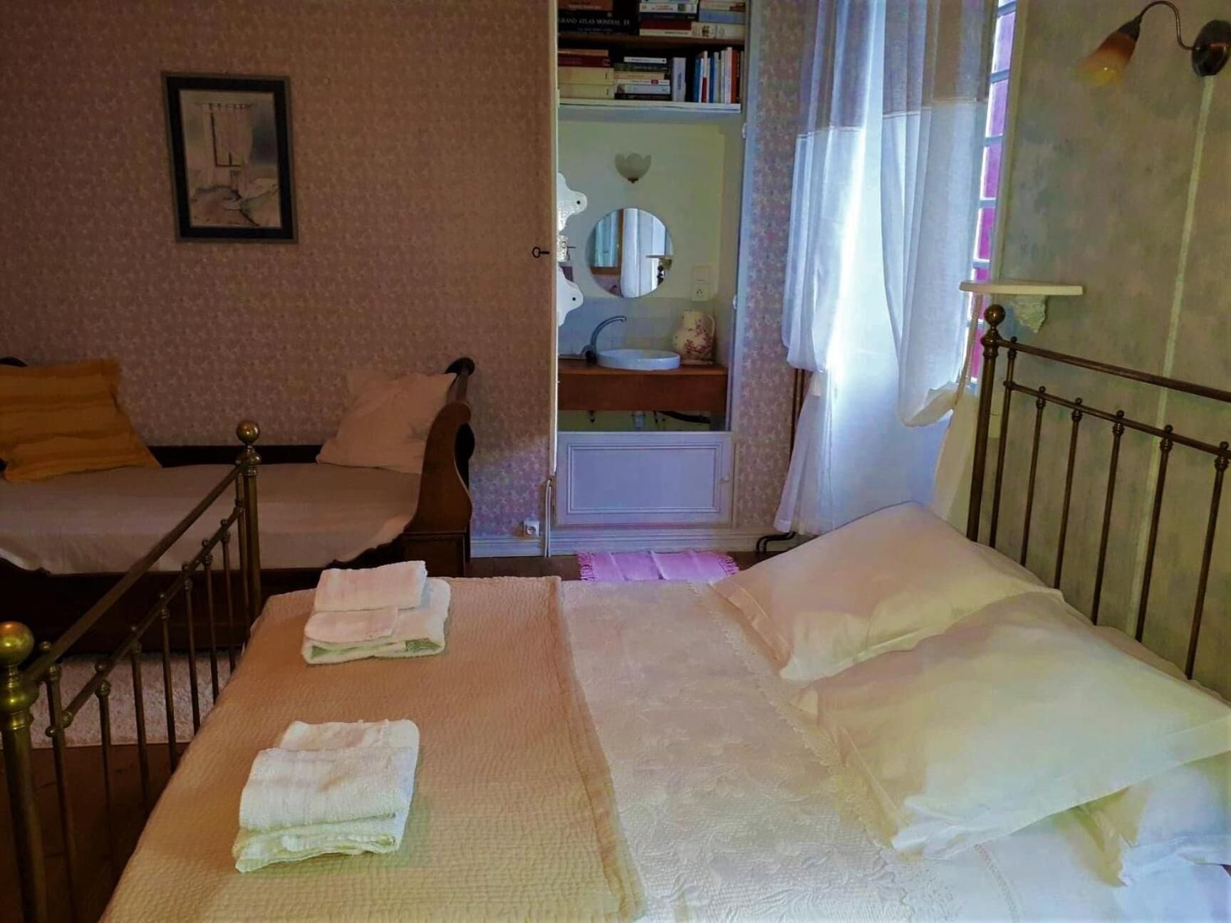Un dormitorio con dos camas, una mesita de noche, un espejo, una estantería y una ventana con cortinas.