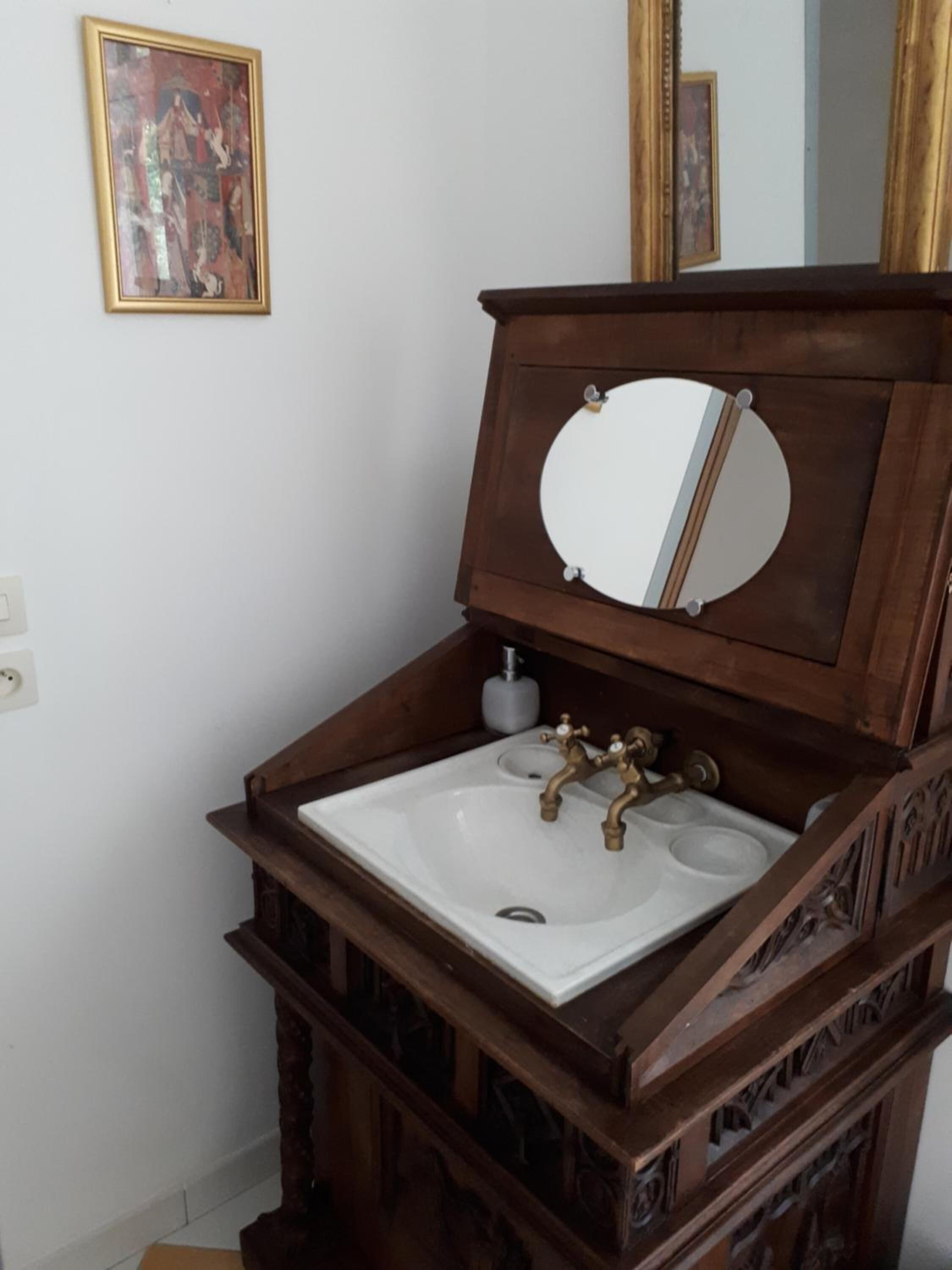 Un tocador de madera con un lavabo blanco, dos grifos y un espejo.