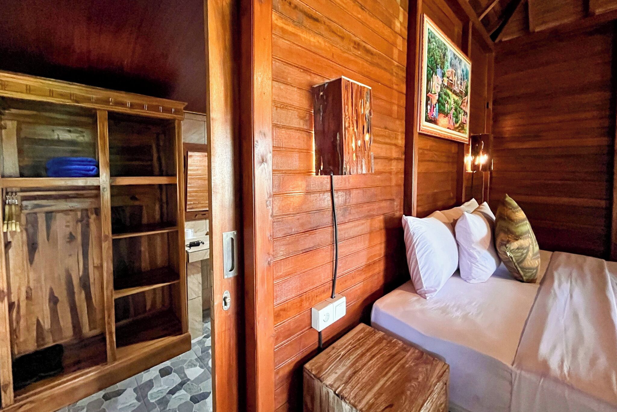 A wooden room with a bed, a wooden cabinet, and a painting on the wall.