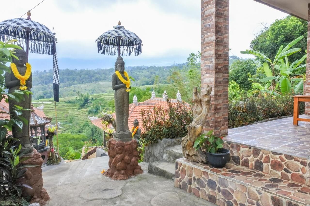 Un espacio al aire libre tranquilo con estatuas de piedra, un patio con baldosas y vistas a campos escalonados.