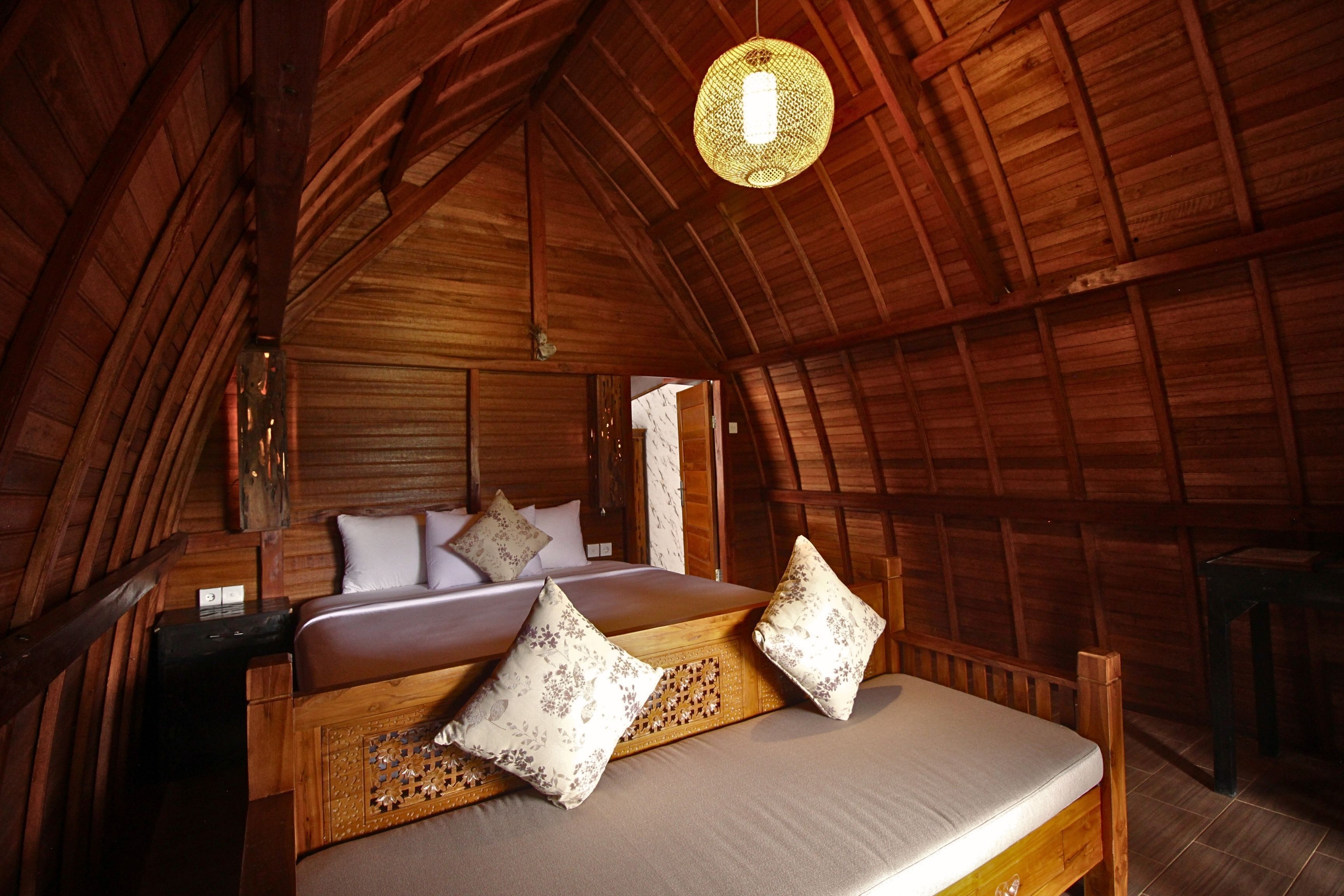 Una habitación acogedora con techo de madera, una cama, almohadas y una lámpara colgante.