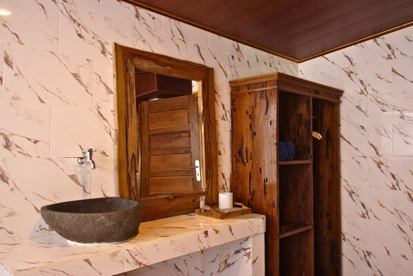 Un baño con pared de azulejos de mármol, un mueble de madera y una pileta de piedra.
