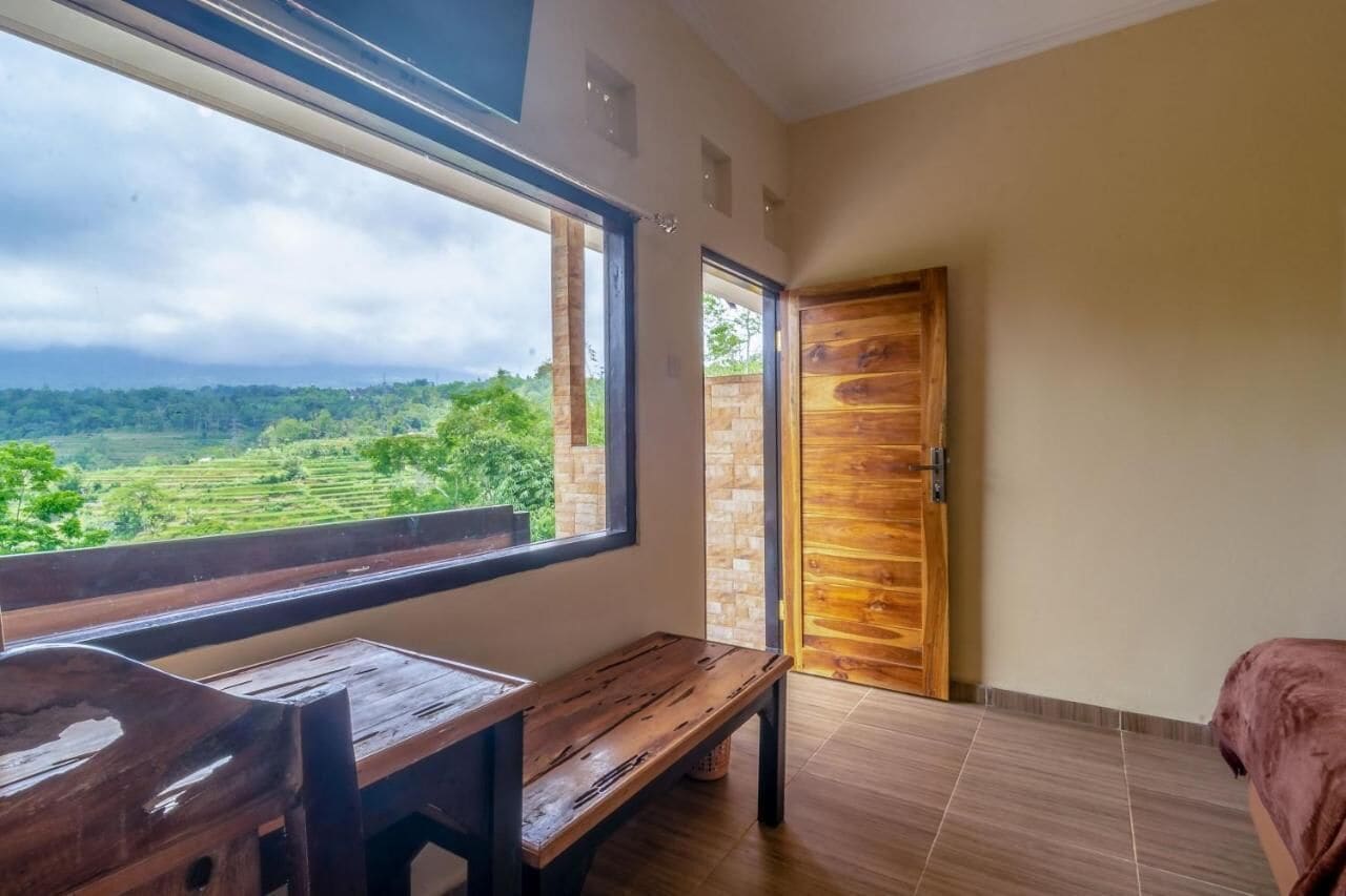 Habitación con un ventanal grande que ofrece vistas a un paisaje verde, un banco de madera y una puerta con diseño de panel de madera.