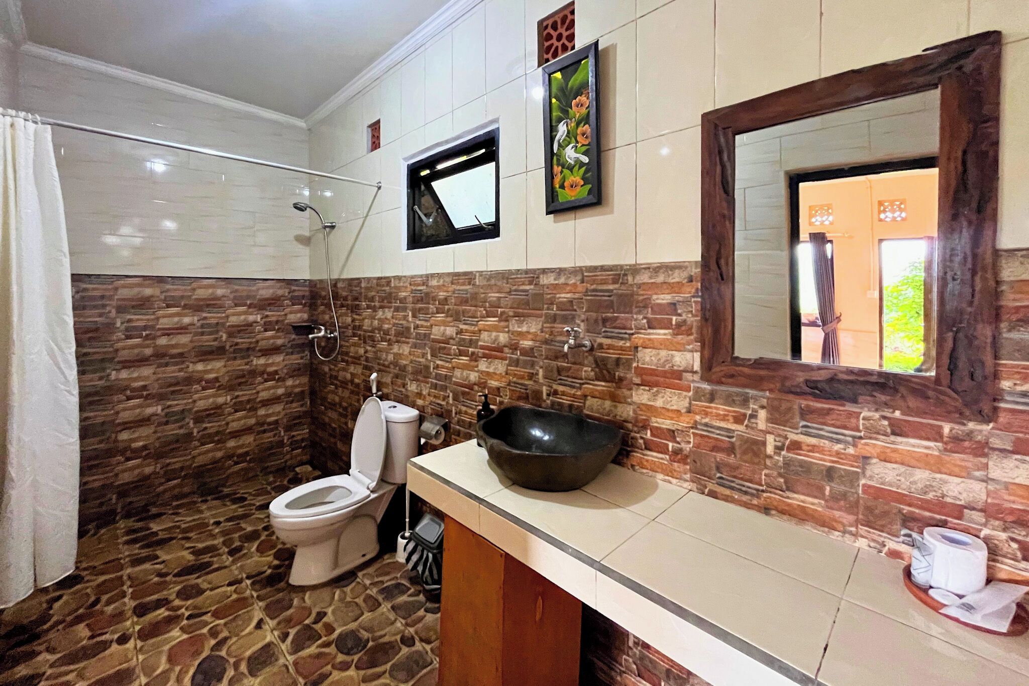 A bathroom with a stone floor, a toilet, a sink with a large basin, and a mirror with a wooden frame.