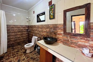 A bathroom with a stone floor, a toilet, a sink with a large basin, and a mirror with a wooden frame.