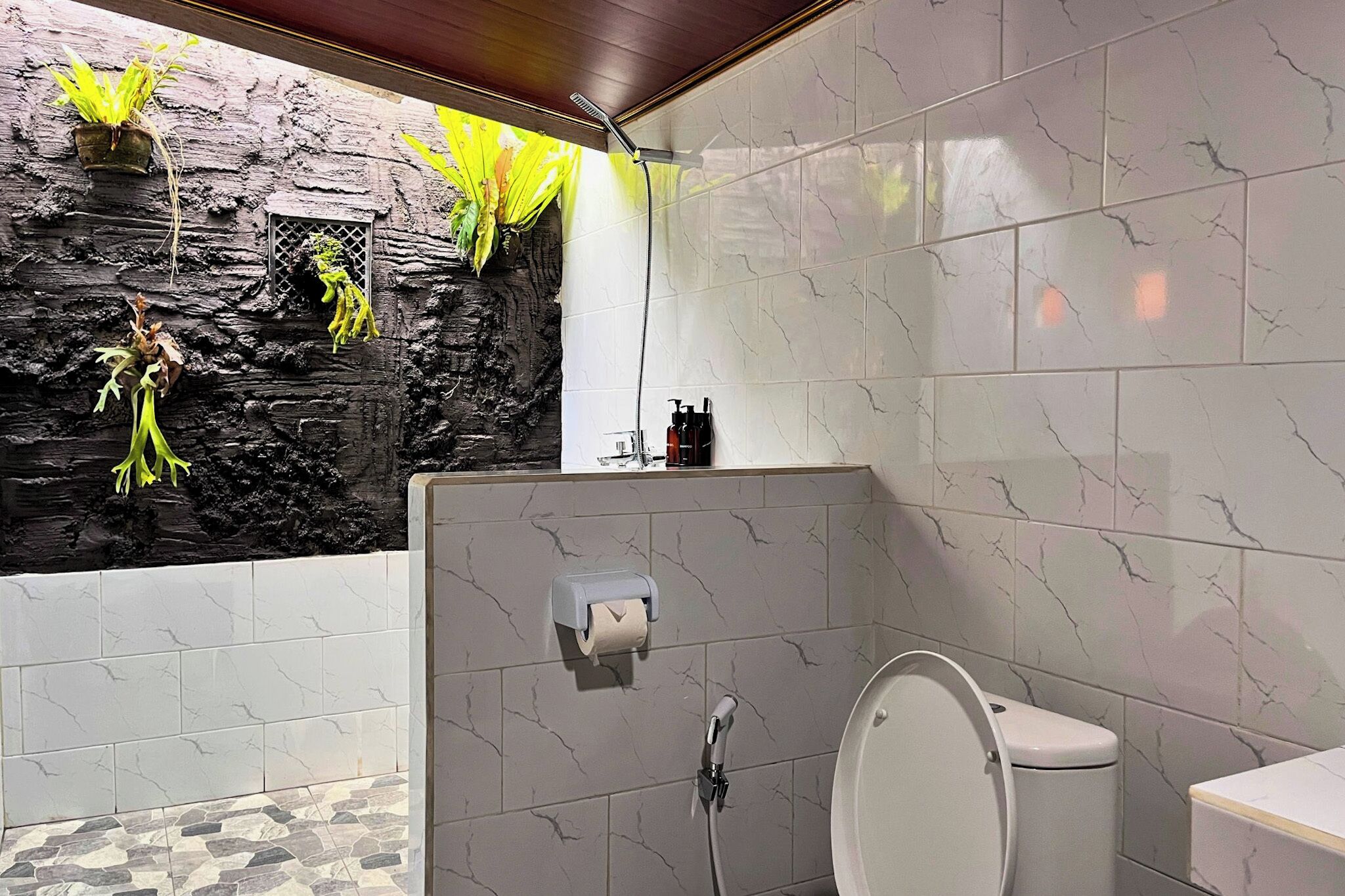 A bathroom with a stone wall, a shower, a toilet, and a sink.