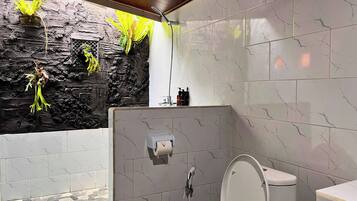 A bathroom with a stone wall, a shower, a toilet, and a sink.