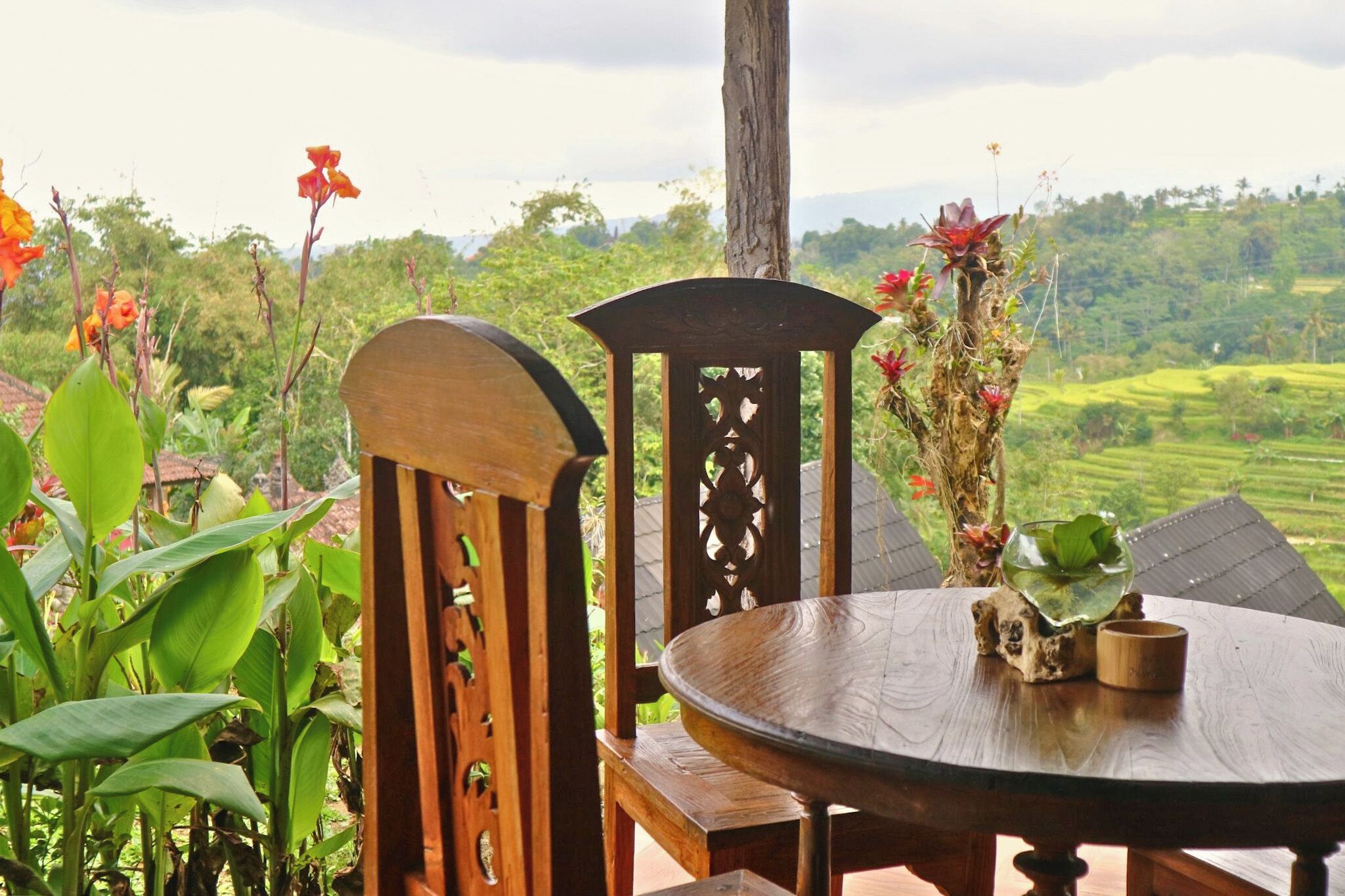 A wooden table and chairs set outdoors with a view of lush greenery and terraced fields in the background.