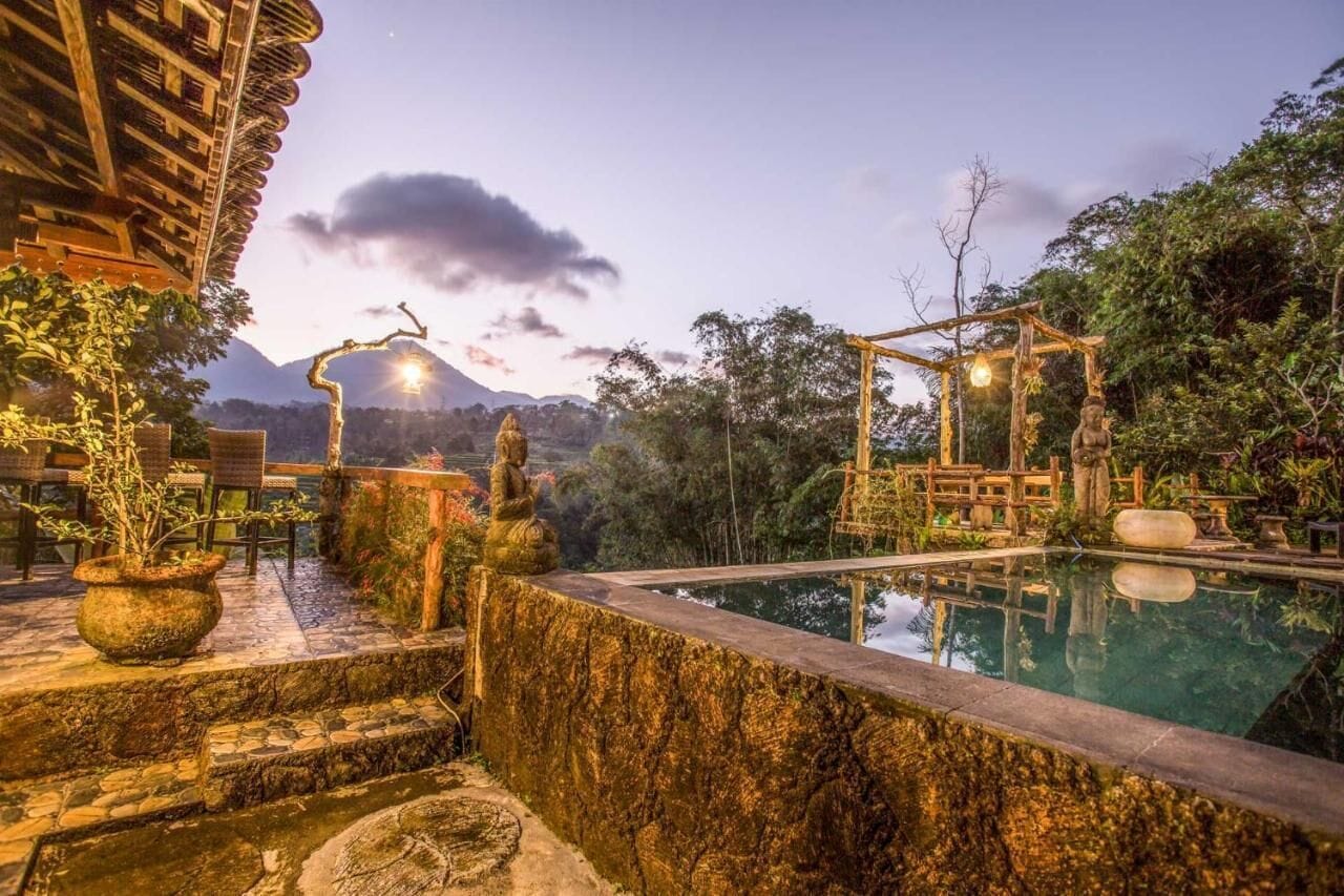 Un área de piscina tranquila con escalones de piedra, un quiosco de madera y montañas al fondo.
