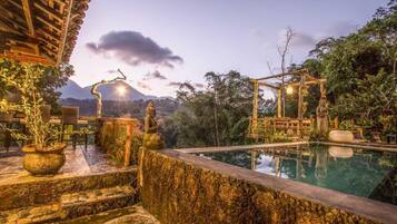 Un área de piscina tranquila con escalones de piedra, un quiosco de madera y montañas al fondo.