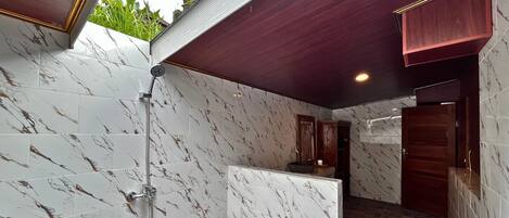 A bathroom with marble tiles, a shower, and a wooden door.