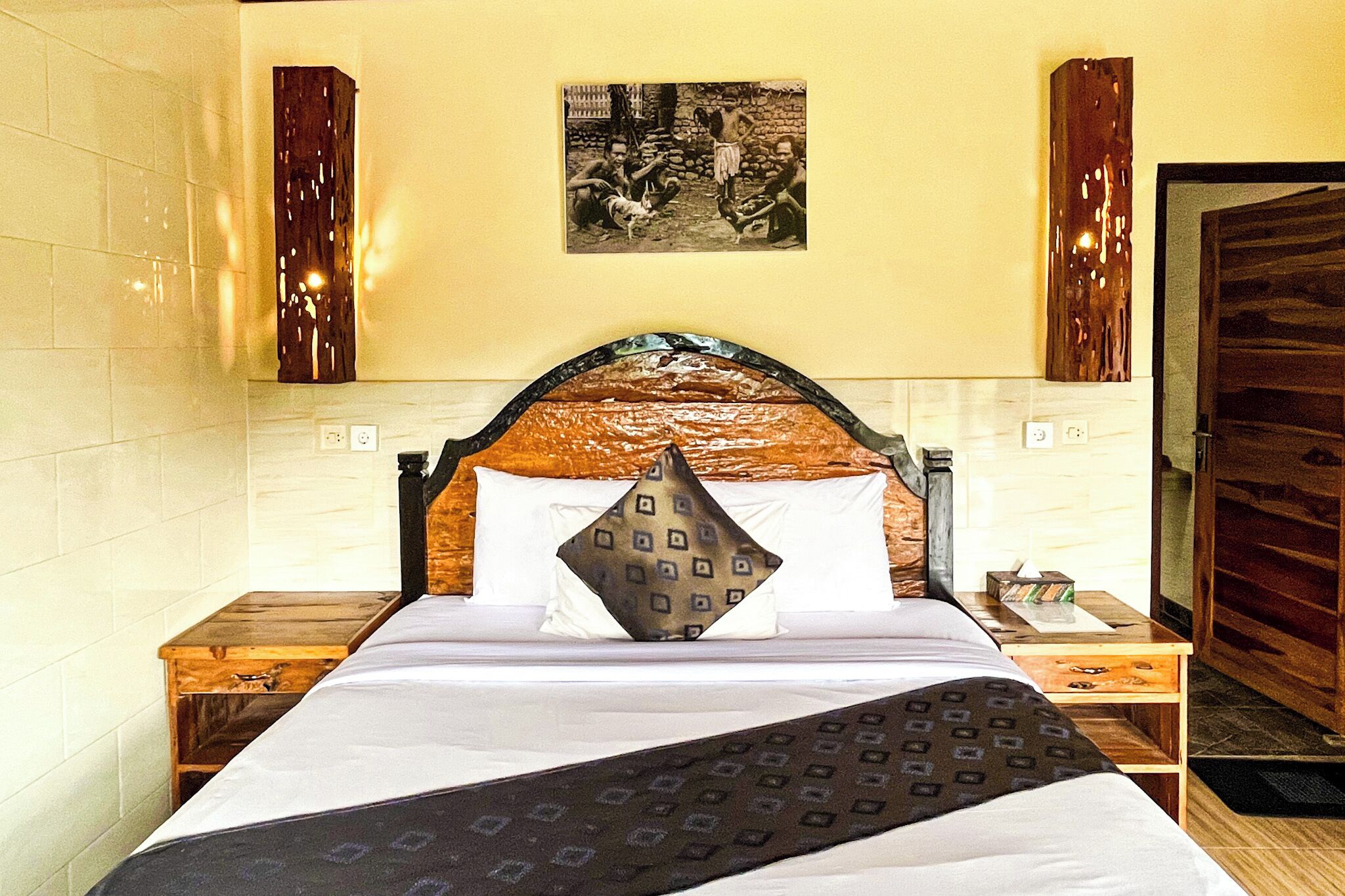 A neatly made bed with a patterned bedspread and pillows, a wooden headboard, and a nightstand with a lamp.