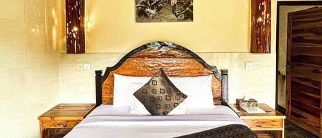 A neatly made bed with a patterned bedspread and pillows, a wooden headboard, and a nightstand with a lamp.