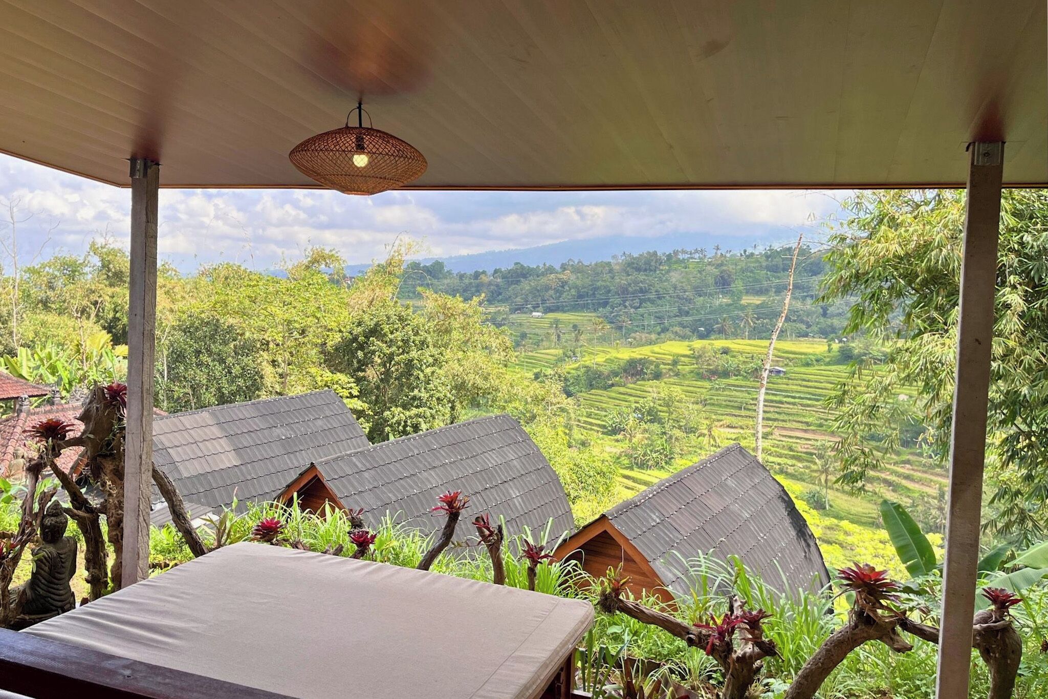 A covered outdoor area with a view of terraced fields and a small building with a sloped roof.