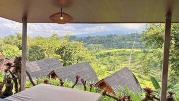 A covered outdoor area with a view of terraced fields and a small building with a sloped roof.