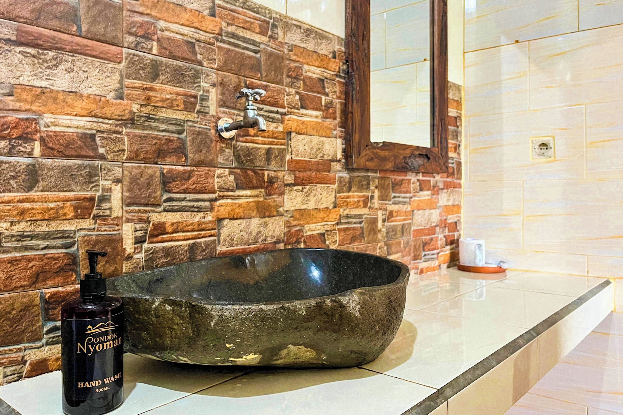 A bathroom with a stone wall, a black basin, and a hand soap dispenser.
