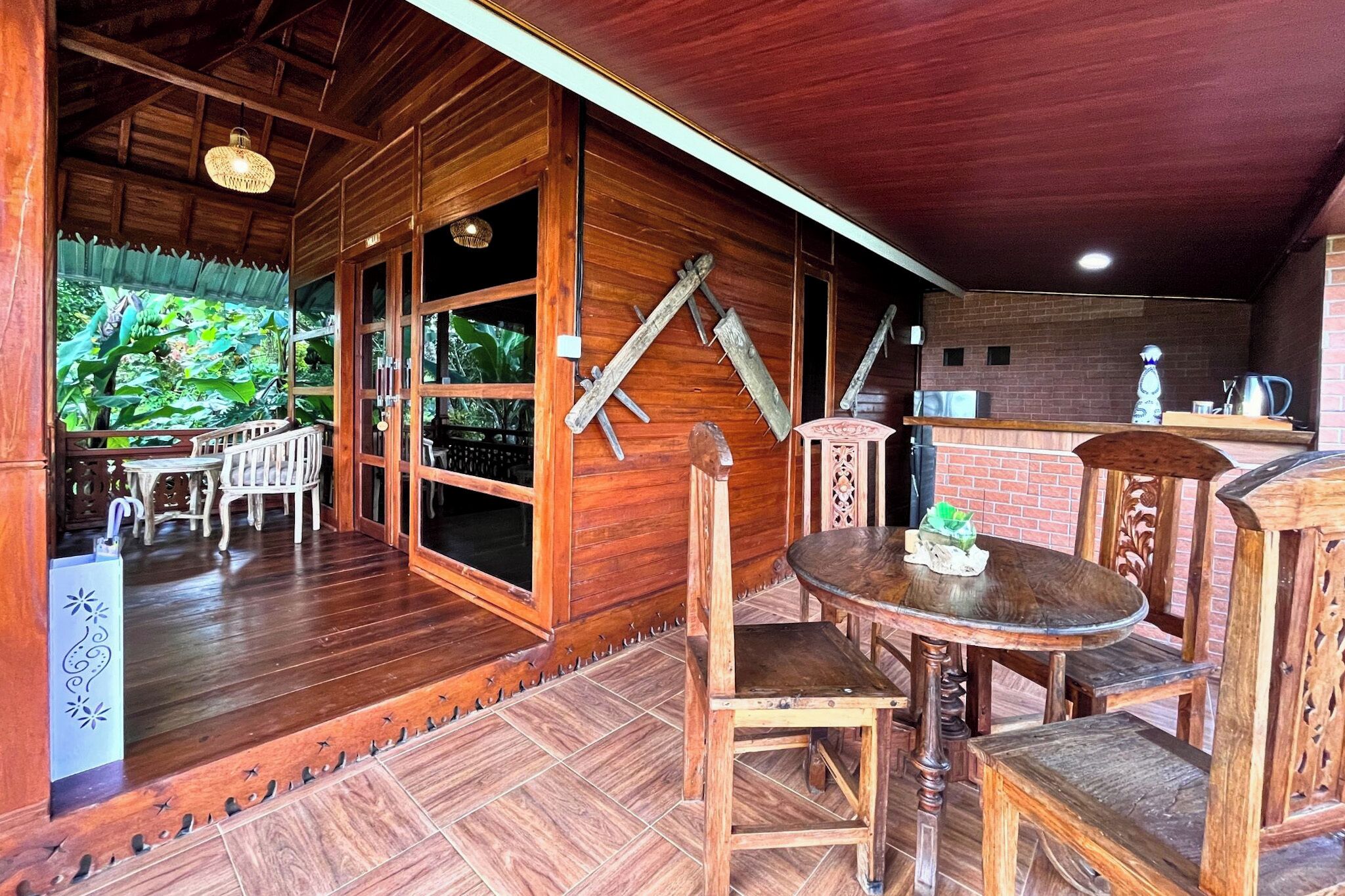 A wooden interior with a dining area, a kitchen, and a view of greenery outside.