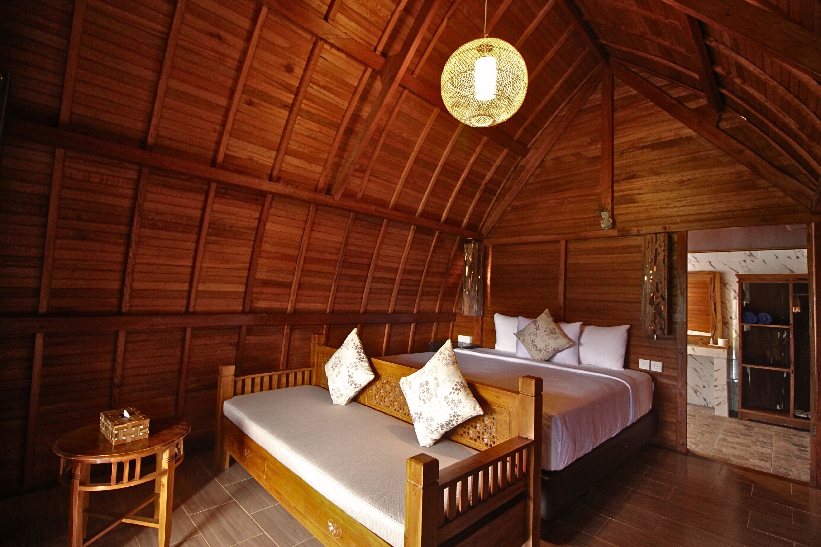 Una cabaña de madera con una cama, una mesita y una lámpara colgante.