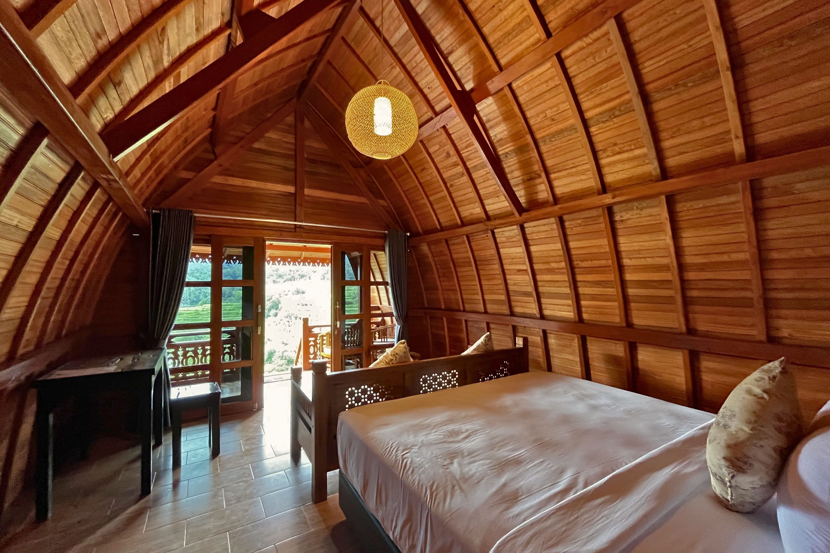 A cozy, wooden-roofed room with a bed, a desk, and a chair.