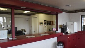 A reception area with a red counter, a computer, a trash bin, and a refrigerator. - Executive Inn Odessa (Odessa)