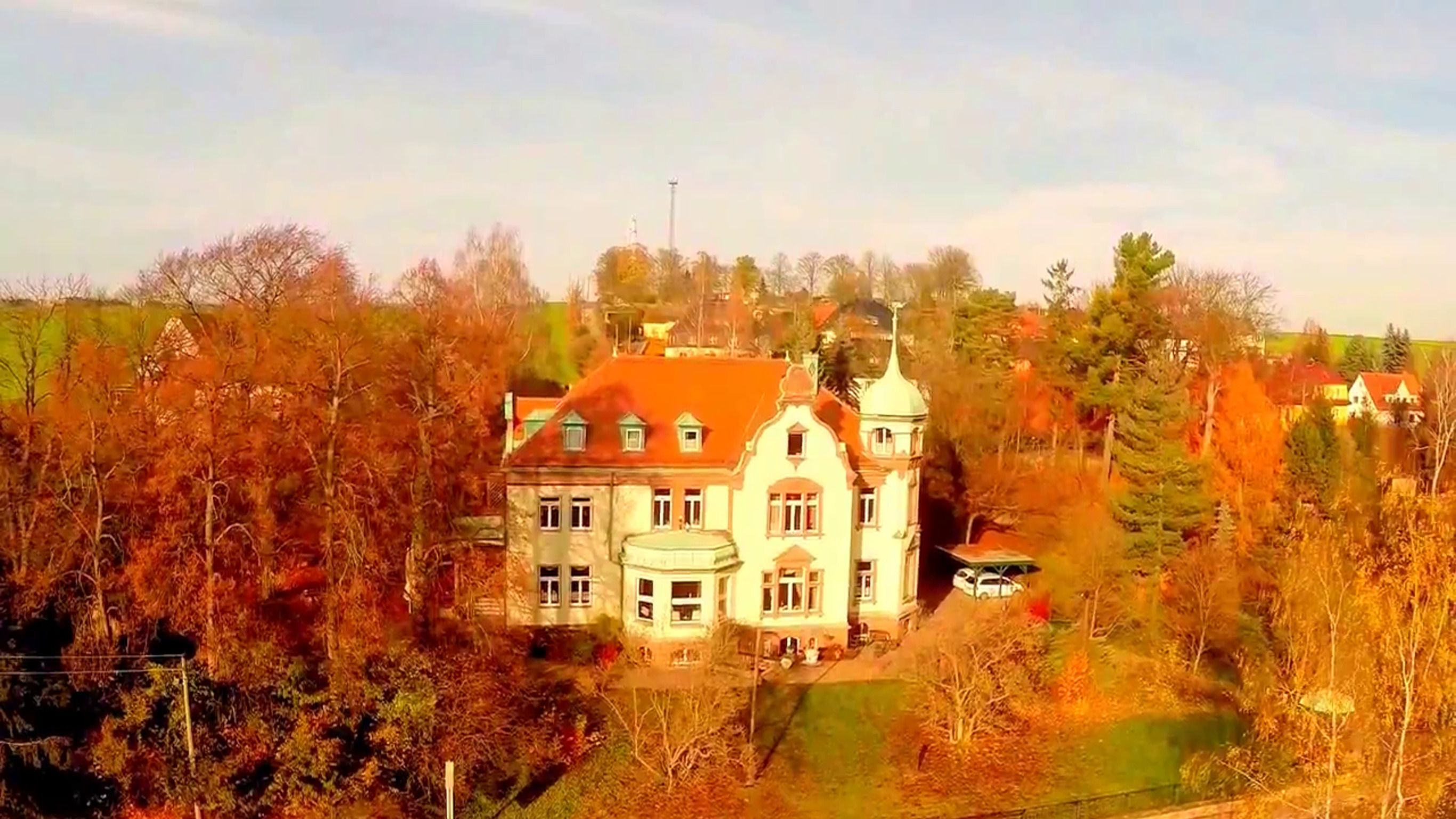 Ein großes, historisches Gebäude mit zahlreichen Fenstern und einem markanten Turm, umgeben von Bäumen und weiteren Gebäuden.