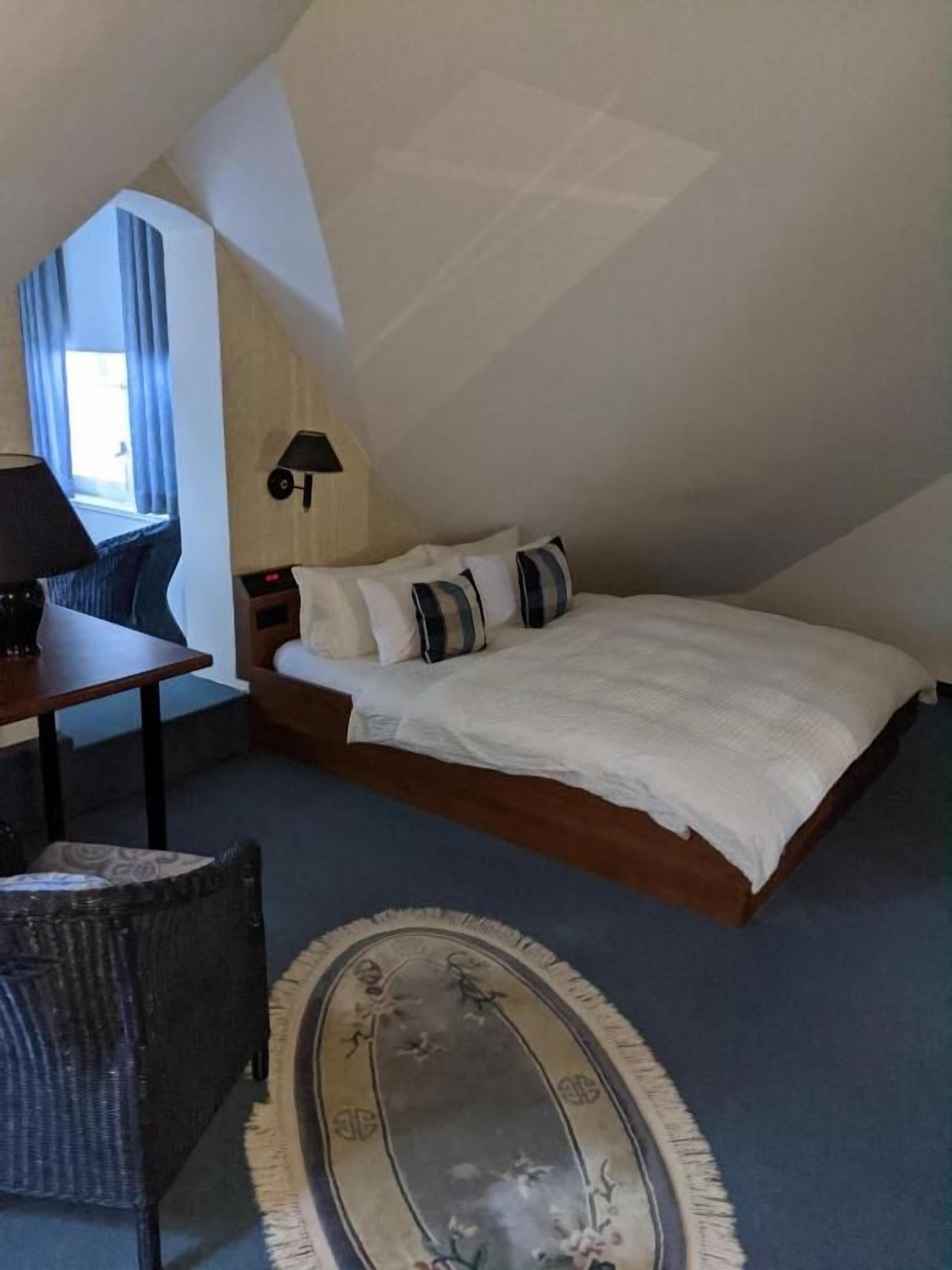A bedroom with a bed, a nightstand, a lamp, and a chair.