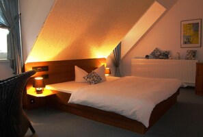 Une chambre avec un plafond en pente, un lit avec une literie blanche, deux lampes de chevet, un radiateur et une chaise.