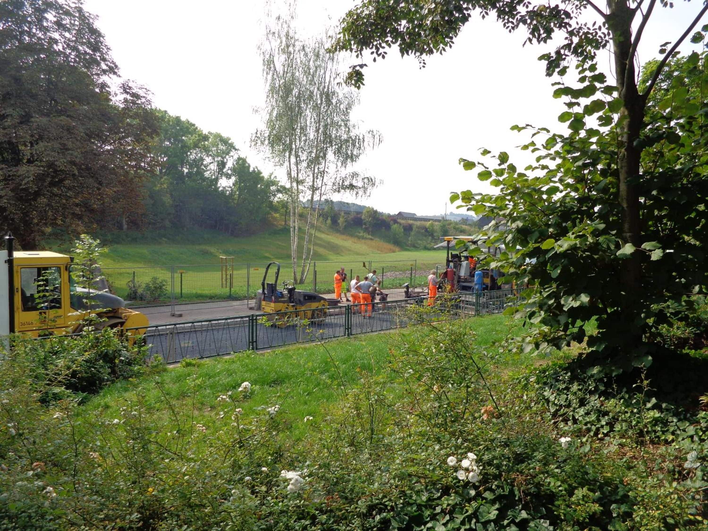 Eine Baustelle mit Arbeitern und Baumaschinen, umgeben von Grünflächen und Bäumen.