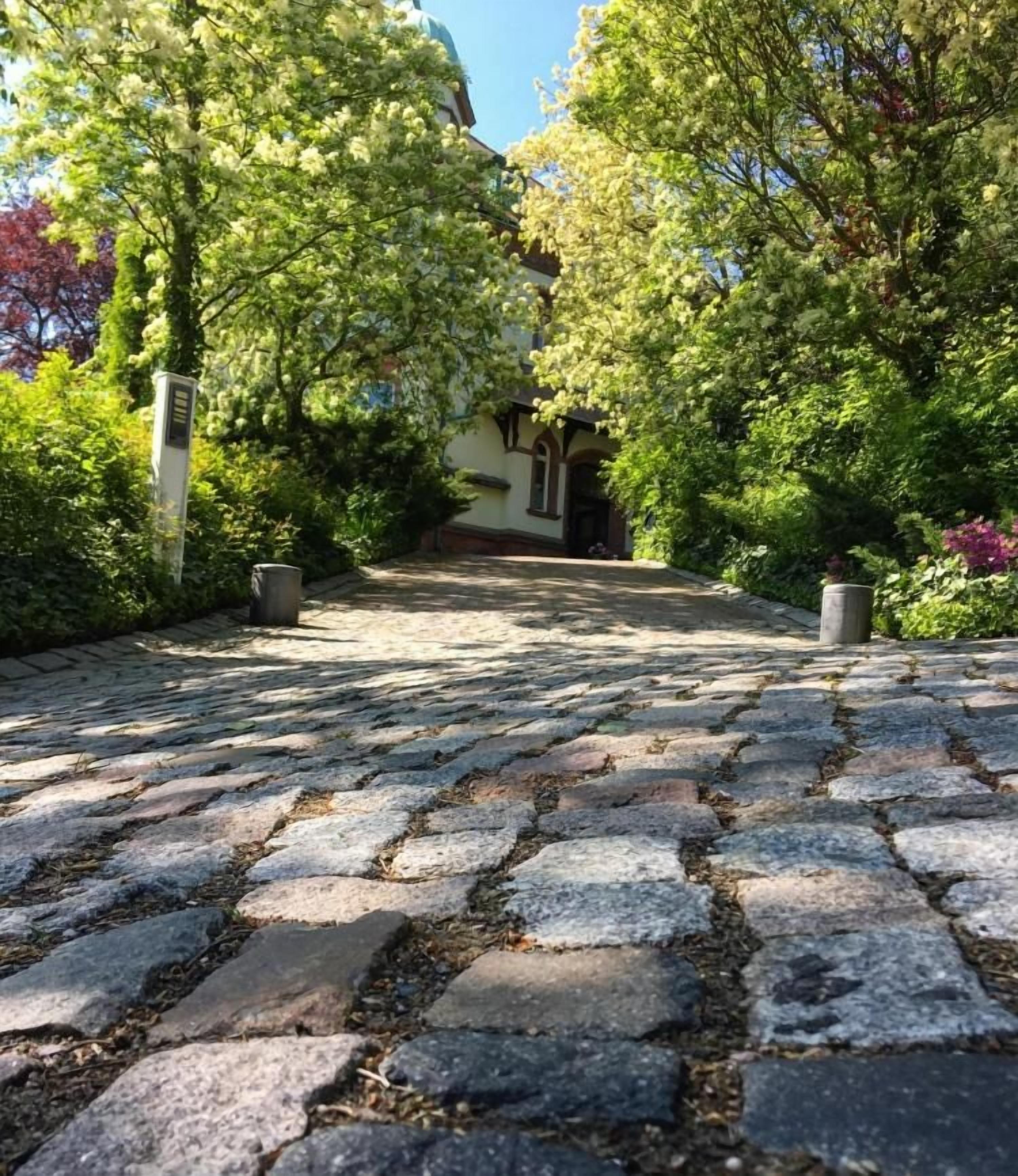 A cobblestone pathway leading to a building with a traditional architectural style, surrounded by lush greenery.