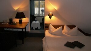 Camera d'albergo con un letto, due lampade da comodino, una scrivania con un telefono, una sedia e un tavolino con un vaso.