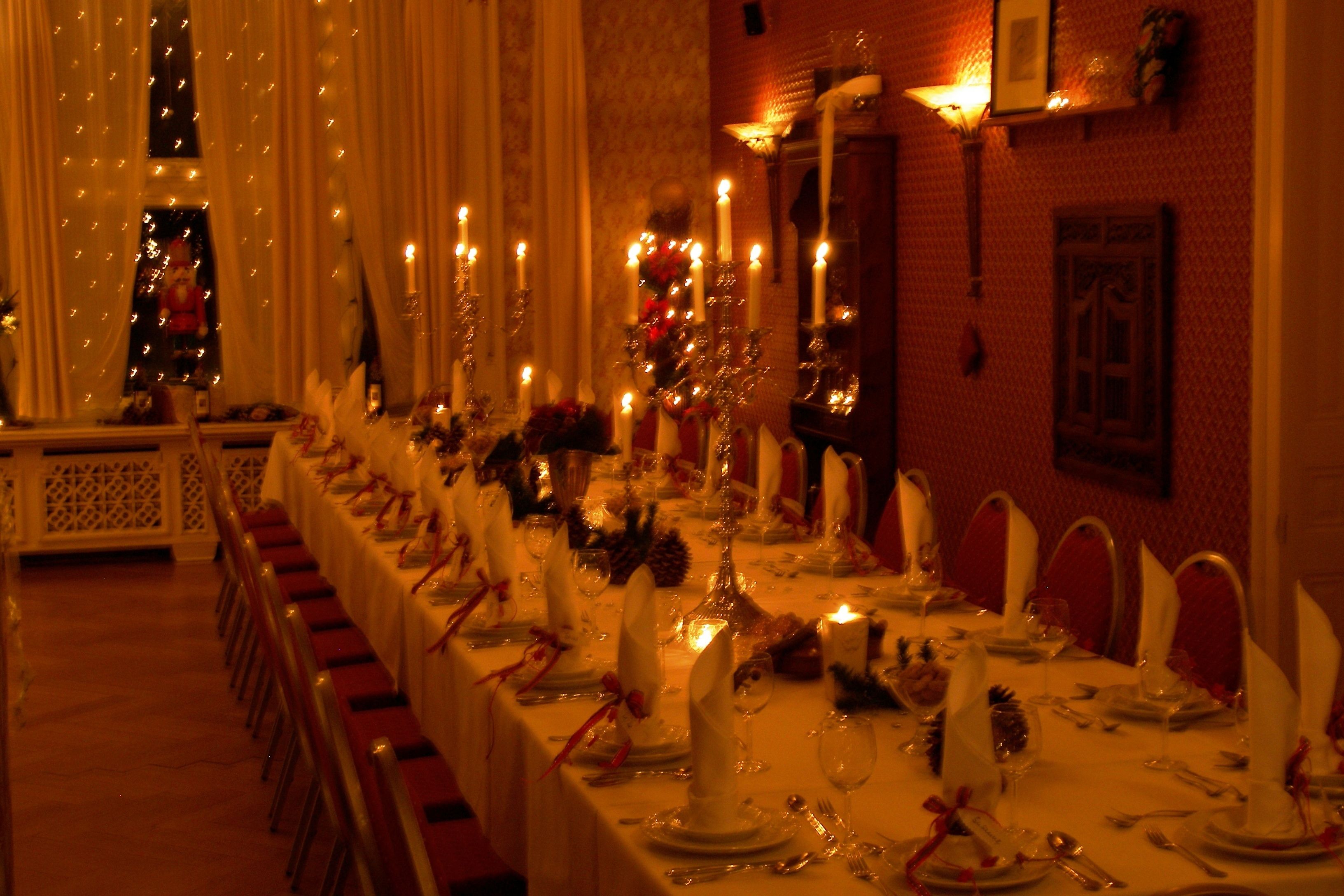 Una larga mesa de banquete dispuesta para un evento formal, con velas, manteles blancos y servilletas rojas.