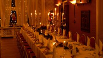 Una larga mesa de banquete dispuesta para un evento formal, con velas, manteles blancos y servilletas rojas.