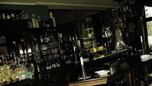 Angolo bar con scaffali pieni di bottiglie e bicchieri, un bancone con una candela e una sedia.