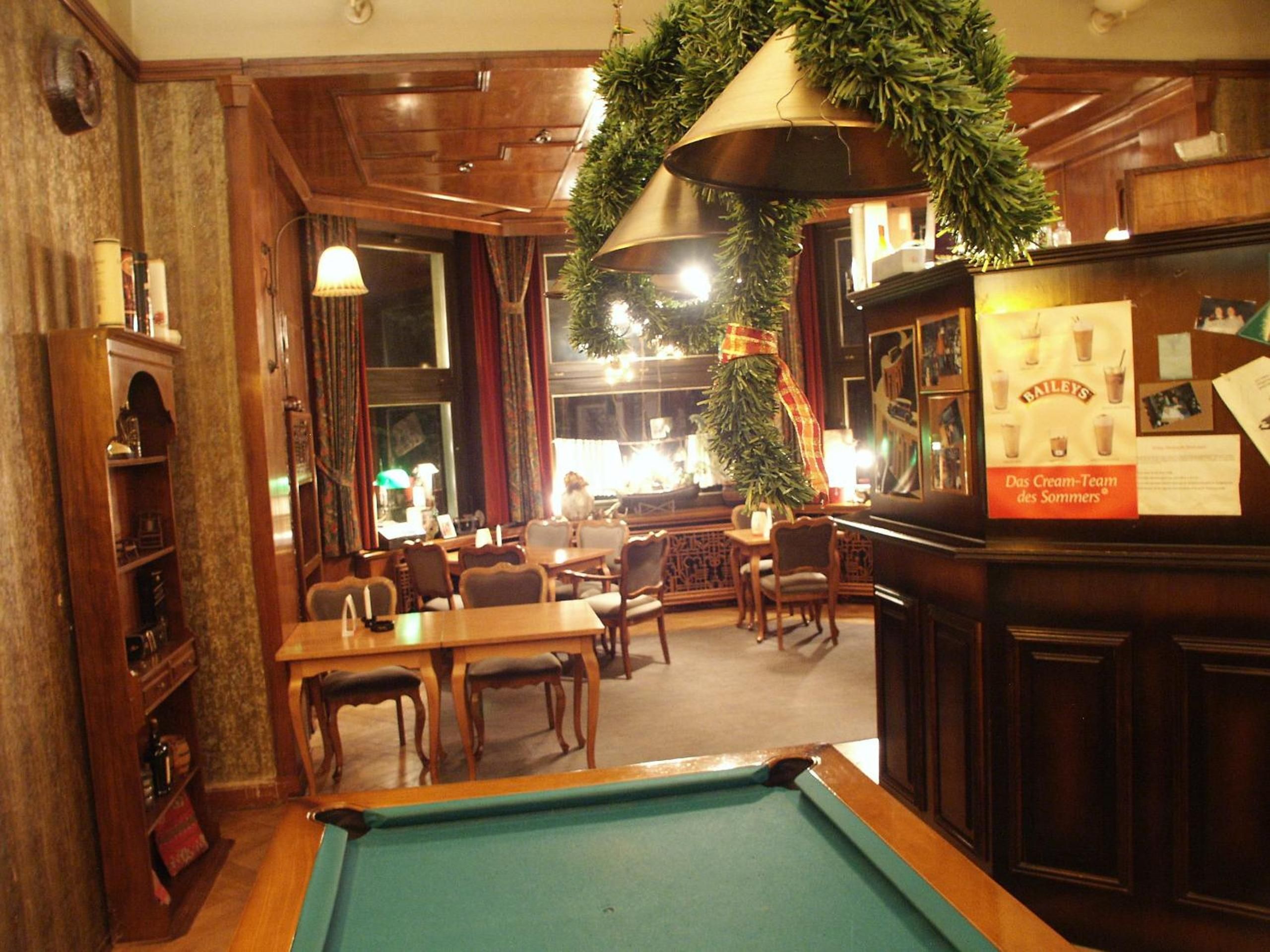 A pool table in a room with wooden furniture, a bar area, and a Christmas wreath decoration.