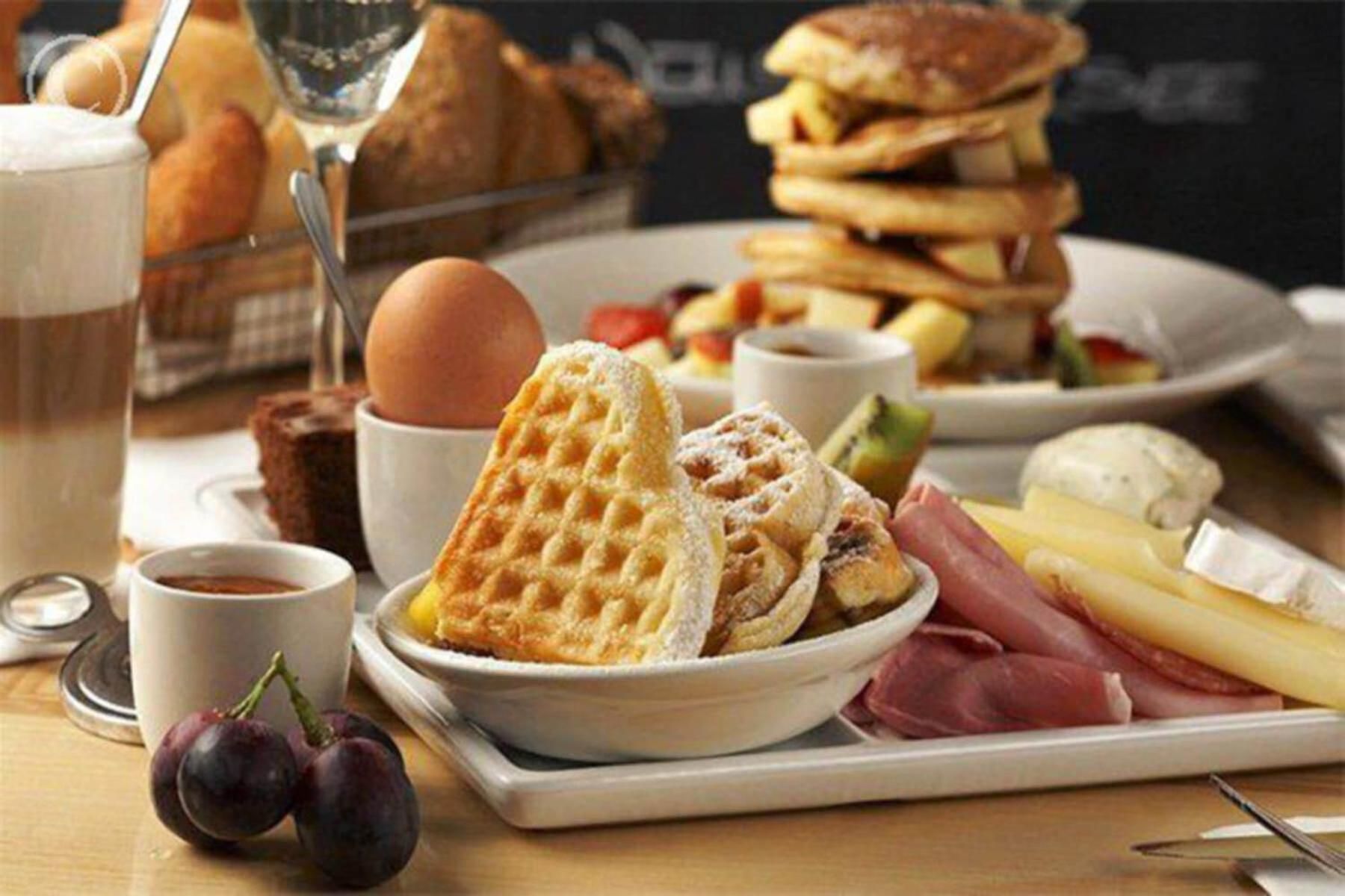 Ein Frühstückstisch mit Waffeln, Käse, Schinken und einer Kaffeetasse.