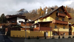 A yellow building with a balcony, a stone wall, and a road in the background. - Haus Alpenblick Mölltal (Flattach)