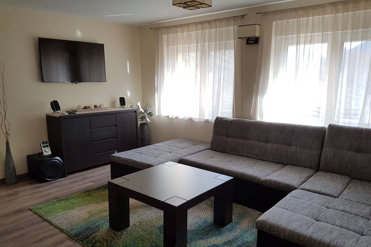 Una sala de estar con sofá, una mesa de centro, un televisor montado en la pared y un aparador.