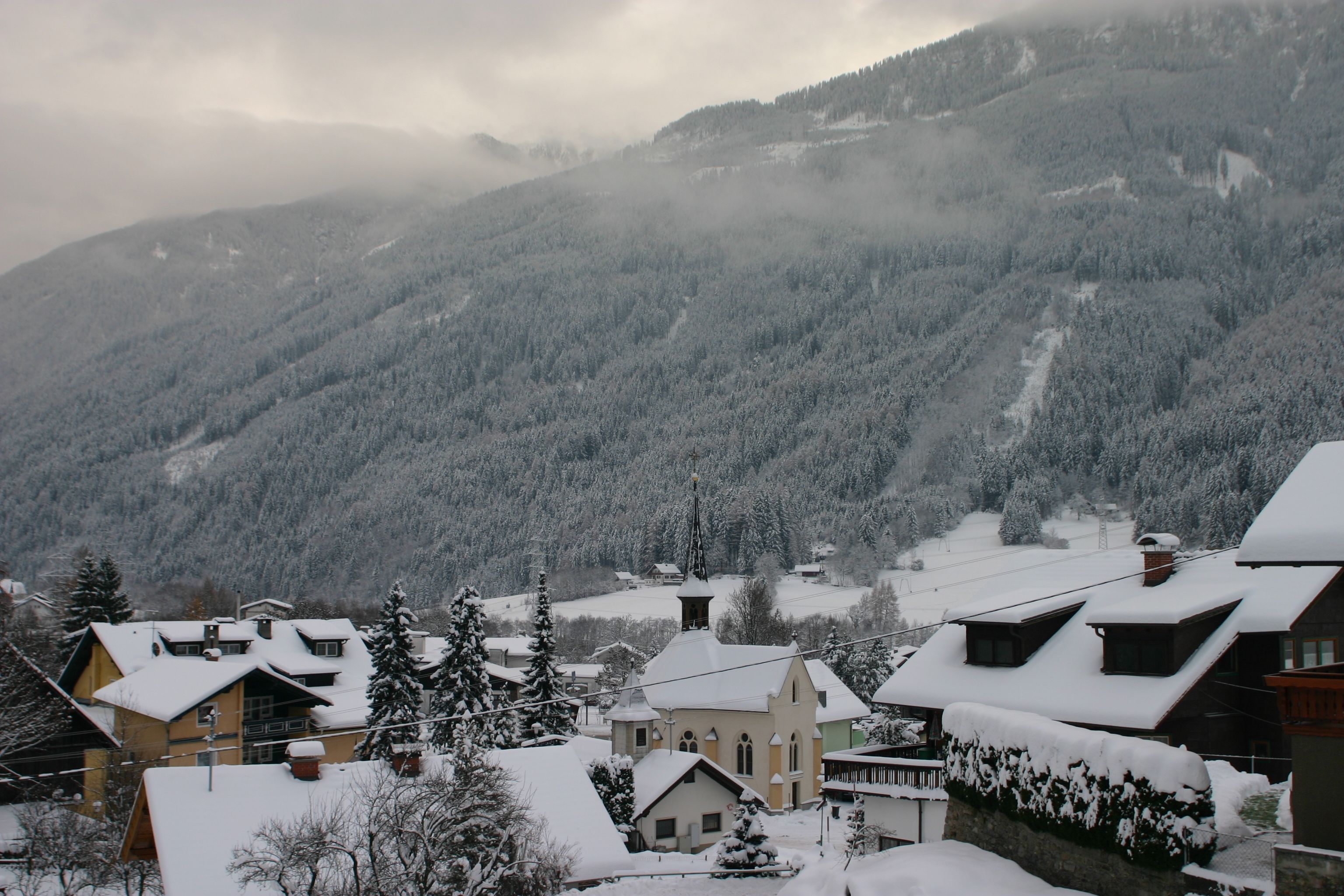 A snow-covered village with traditional houses, a church, and a mountain backdrop.