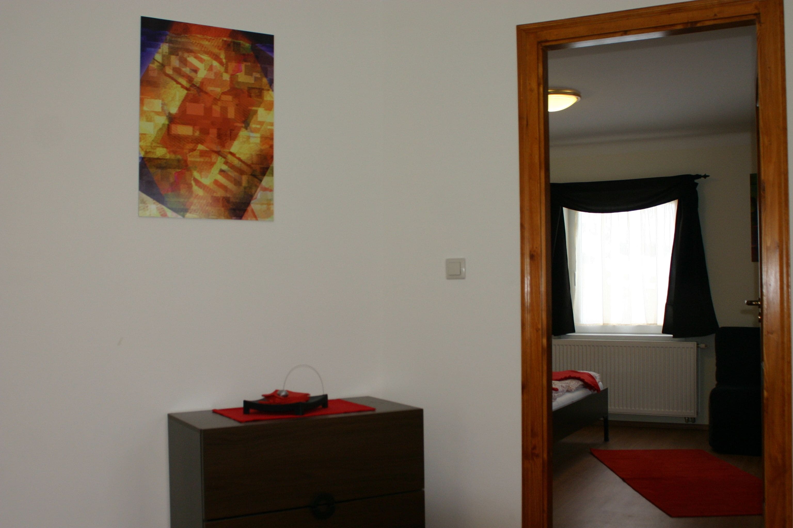 A room with a bed, a dresser, a red rug, and a painting on the wall.