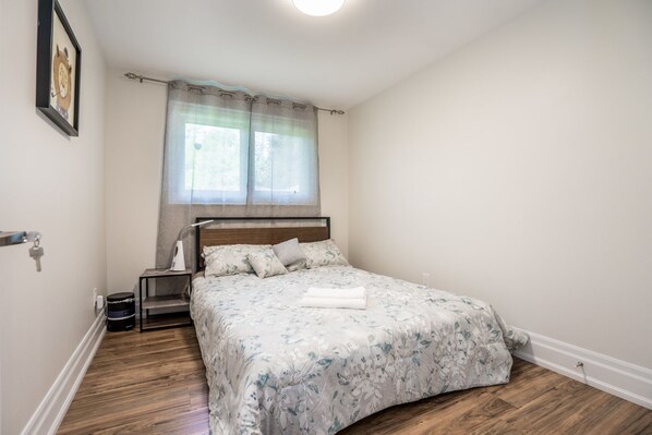 Un dormitorio con cama, mesita de noche, lámpara y ventana con cortinas.