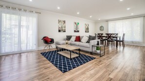 A spacious living room with a grey sofa, a coffee table, and a dining area with wooden chairs and a table. - Entire Bungalow 5 Bedrooms (Markham)
