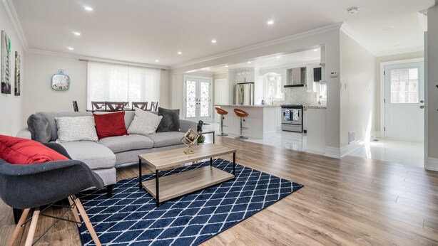 A spacious living area with a grey sofa, red and white cushions, a wooden coffee table, and a blue patterned rug. - Entire Bungalow 5 Bedrooms (Markham)