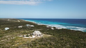 Une propriété située sur la côte, comprenant plusieurs bâtiments, dont une grande maison blanche dotée d’un balcon, entourée d’une végétation luxuriante et offrant une vue sur l’océan.