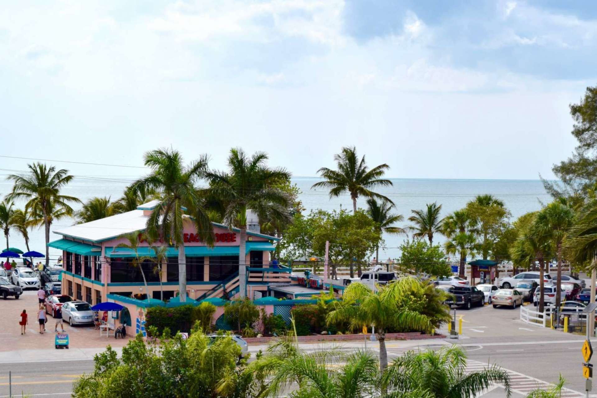 A beachfront hotel with a prominent red sign, a covered outdoor seating area, and a view of the ocean.