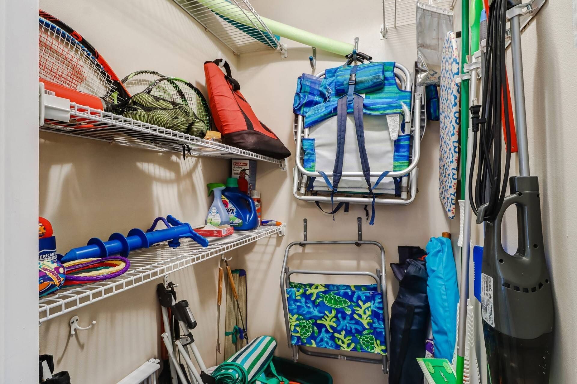 A compact storage area with shelves holding various items like cleaning supplies, a blue towel with a turtle pattern, and a red life jacket.