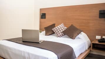 Una cama bien tendida con una computadora portátil, almohadas y una mesita de noche con una cámara.